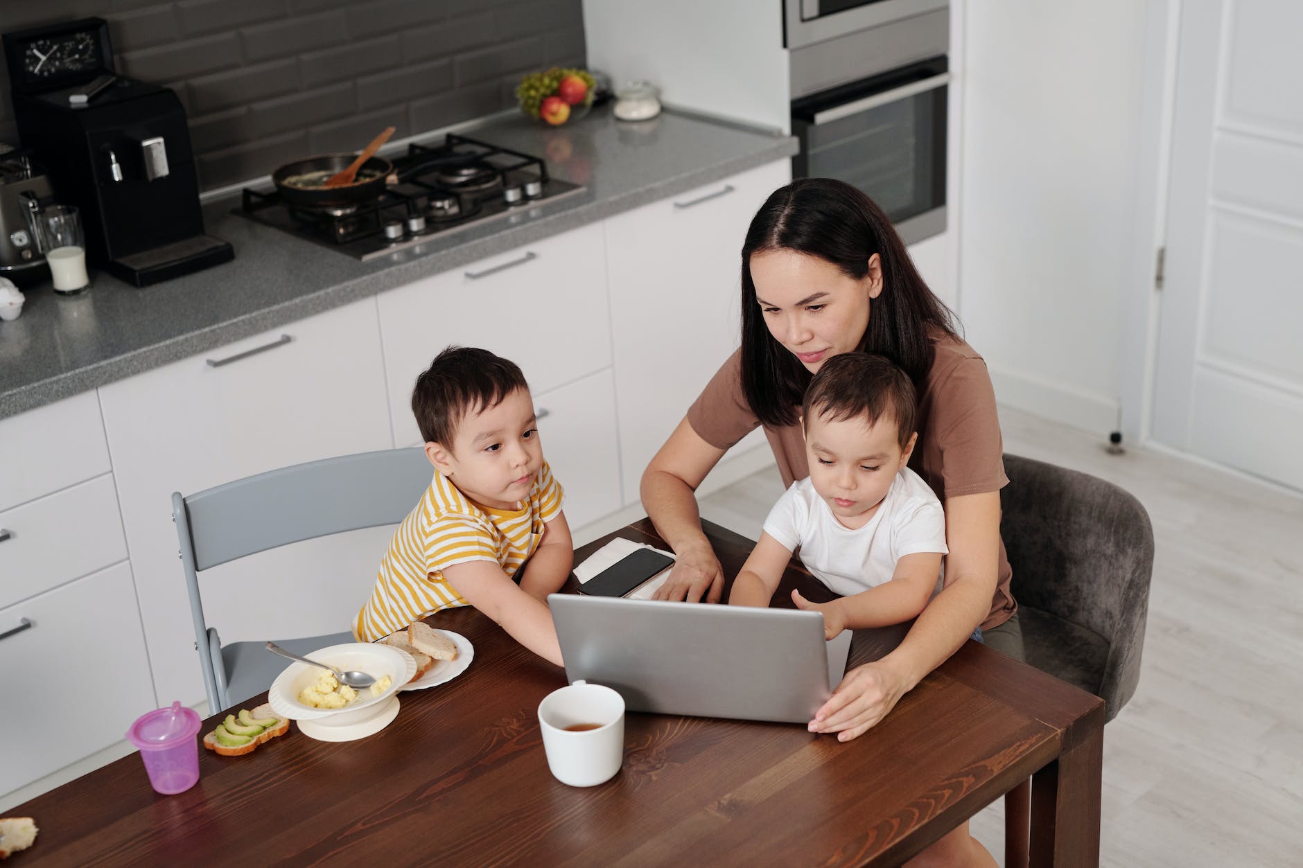 a woman in brown shirt using her laptop with her kids while sitting near the wooden table